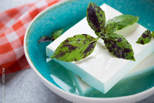 Photography Closeup of a bowl with blocks of feta cheese in a brine and fresh green basil le
