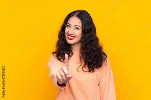 Spanish Chinese woman over isolated yellow background showing and lifting a finger