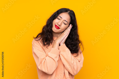 Spanish Chinese woman over isolated yellow background making sleep gesture in dorable expression © luismolinero