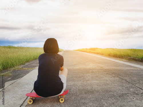 Asian girl sitting on the skateboard looking at sun set