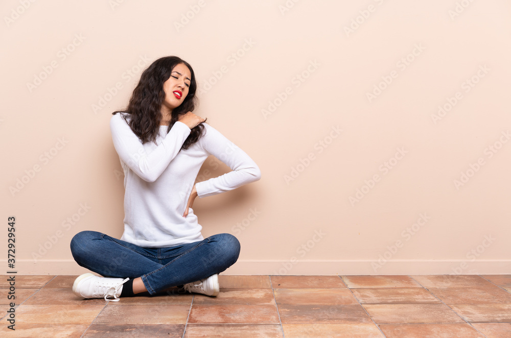 Young woman sitting on the floor suffering from pain in shoulder for having made an effort Young woman sitting on the floor suffering from pain in shoulder for having made an effort