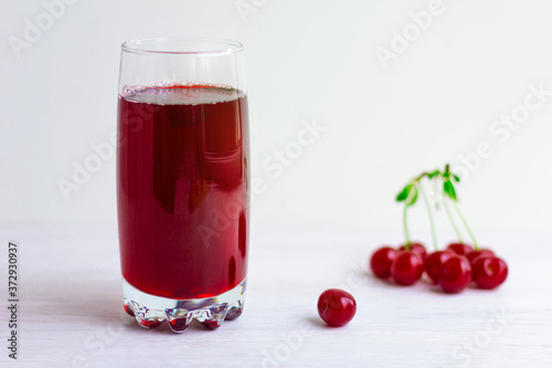 The transparent glass of cherry red juice and berries on light wooden background