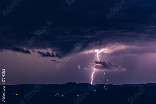 Night landscape on a background of thunderstorms. Rural silhouette and clouds with lightning flashes