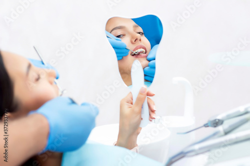 Fototapeta Naklejka Na Ścianę i Meble -  young women checks her teeth in the mirror. Young woman in the dentists office. New dental implants.
