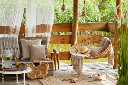 Φωτογραφία Interior design of  summer gazebo by the lake with stylish rattan armchair, coffee table, sofa, pillows, plaid and elegant accessories in modern decor