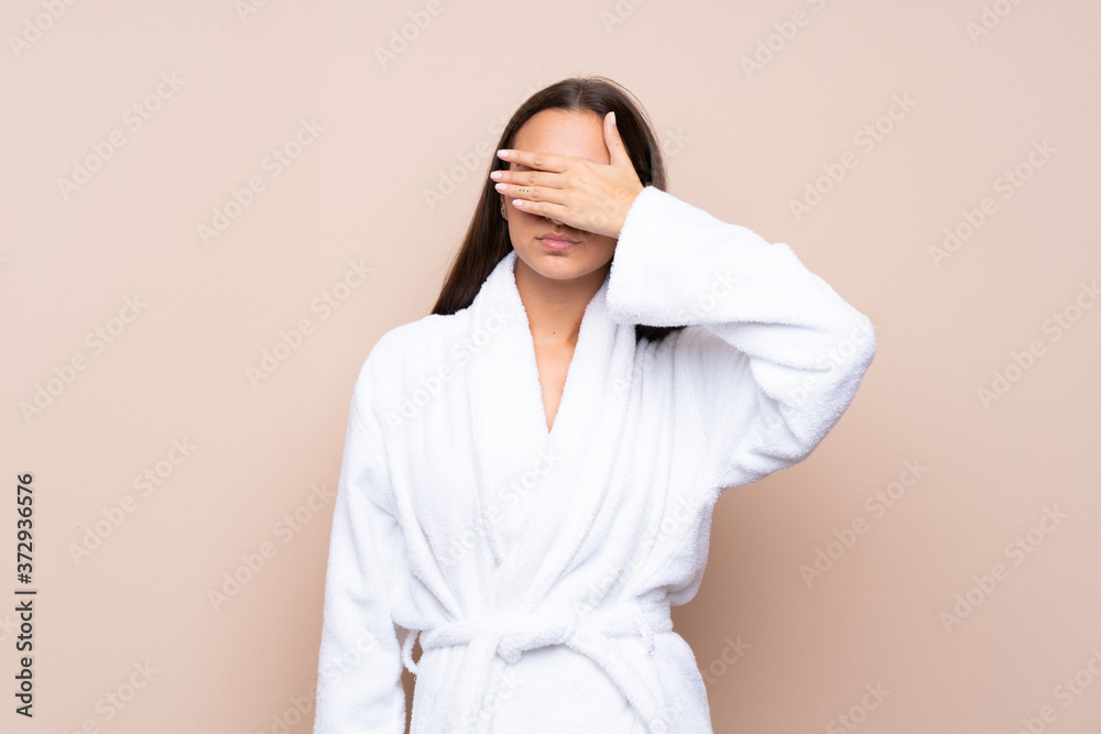 Young girl in a bathrobe over isolated background covering eyes by hands Young girl in a bathrobe over isolated background covering eyes by hands