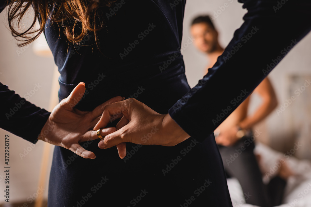 Selective focus of woman with hands behind back taking off wedding ring near shirtless man in bedroom - obrazy, fototapety, plakaty 