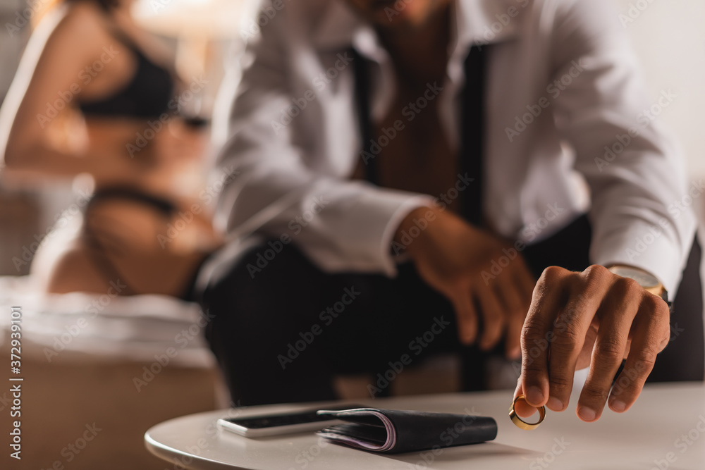 Selective focus of man putting wedding ring near wallet and smartphone on coffee table near woman in lingerie on bed