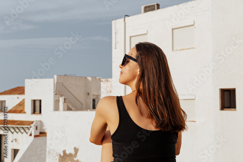 A traveler brunette girl is looking at the white buildings.Woman looking on the city. Back view of beautiful giel wearing sunglasses photo