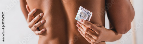 Fotografi Panoramic shot of woman touching back of muscular man and holding condom at home