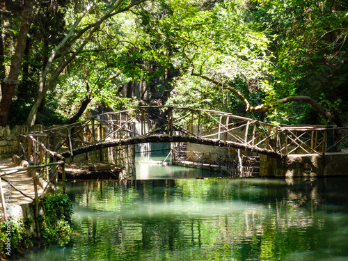 Calm pond of water reflecting trees and wood with river waterfall and bridge