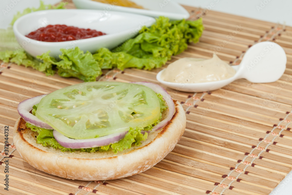 Slice Of Bread For Hamburger With Vegetables: Green Tomato, Lettuce And Onion Rings; Ready To Assemble The Burger. Slice Of Bread For Hamburger With Vegetables: Green Tomato, Lettuce And Onion Rings; Ready To Assemble The Burger.