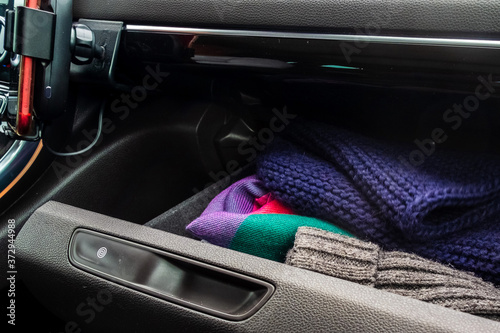 Knitted scarves and hats are in the glove compartment of a car.