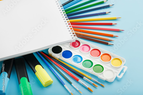 An album for drawing and creativity for school with stationery, a palette of colored paints, markers, brushes and pencils.