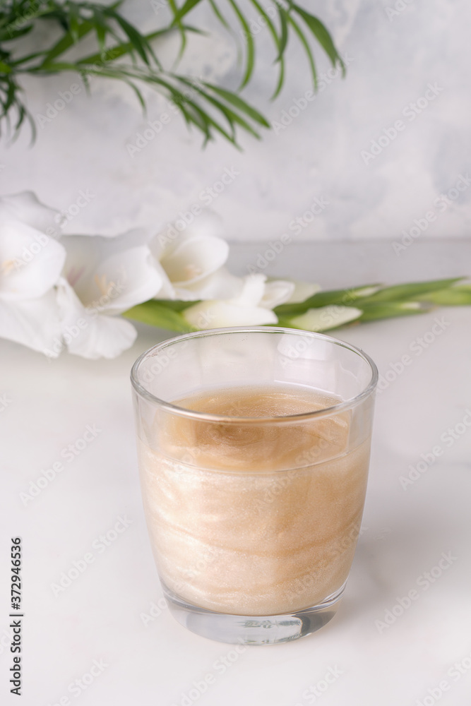 drink with shimmer in a glass on a gray background next to white flowers drink with shimmer in a glass on a gray background next to white flowers