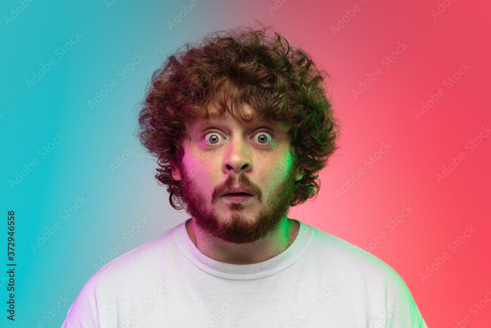 Shocked. Caucasian young man's portrait isolated on gradient studio background in neon light. Beautiful male model in casual style. Concept of human emotions, facial expression, youth, sales, ad. Shocked. Caucasian young man's portrait isolated on gradient studio background in neon light. Beautiful male model in casual style. Concept of human emotions, facial expression, youth, sales, ad.