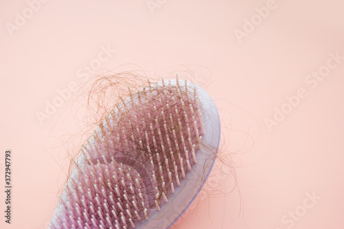 Comb with long woman hair on pink background. Hair loss problem