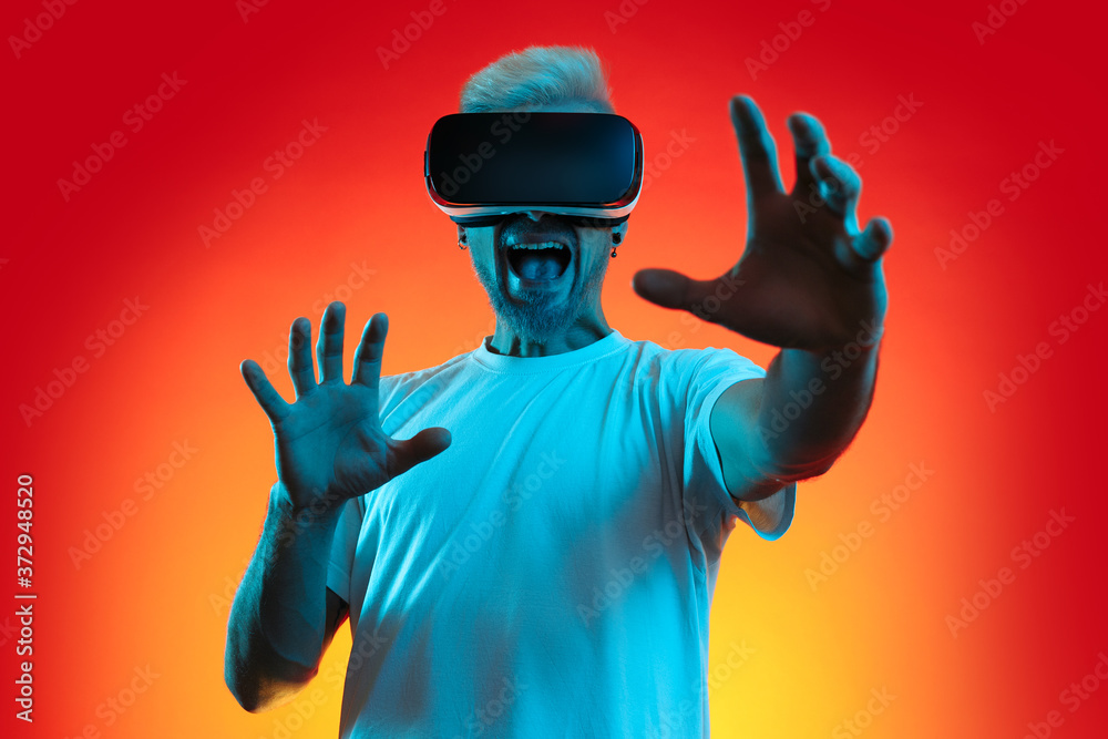 Excited bearded blonde hipster man with blonde hair wearing virtual reality goggles in studio in neon lights.