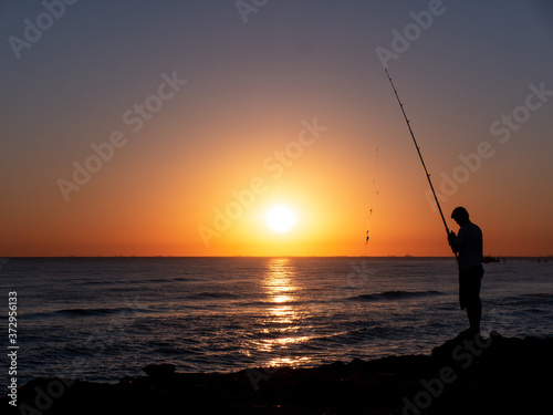 silhouette of fisherman by the ocean in sunrise  A fisherman in sunset at the coast 