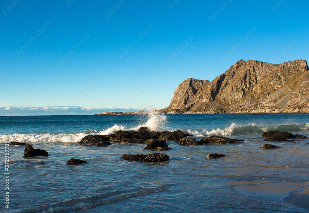 sea splashing on a rock on a beach with mountains in the background coast line North norway blue sky
