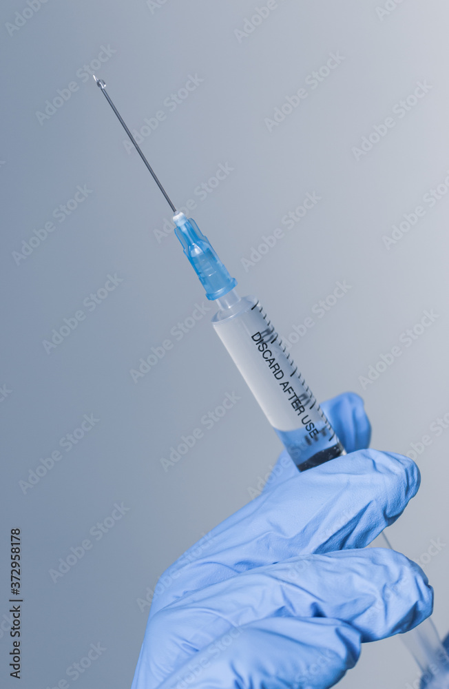 Hand in blue glove holding syringe with copy space. Syringe with sharp needle in hand, vertical. Medical treatment concept. Laboratory backgrouund. Medicare concept. Vaccination concept. 