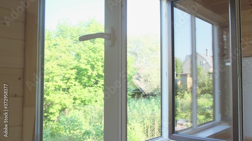 A man closes a white plastic window by the handle.