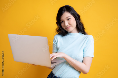young woman using laptop, isolated image on yellow background