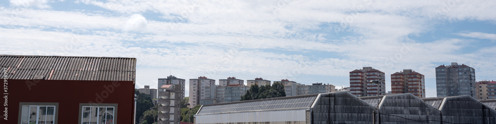Caranza skyline panorama and sunny cirrus cloudy sky. Ferrol city neighborhood towers in banner crop with industrial buildings in foreground. Summer weather with little and soft clouds