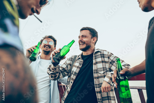 Group of friends celebrating, resting, having fun and party in summer day. Young men drinking beer, talking, laughting. Look happy and cheerful. Festive time, holiday, summertime, unity and friendship © master1305