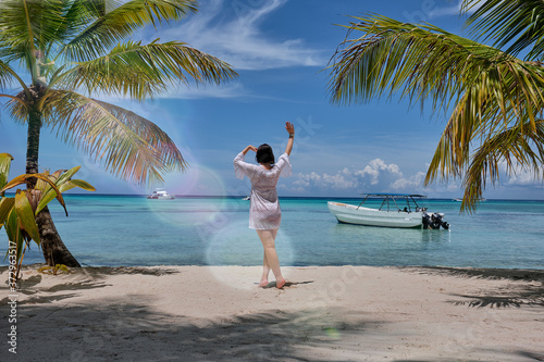 A girl looking horizon standing next to a palm trees on a beach in front of a Caribbean sea 