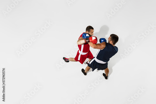 Two professional boxers boxing isolated on white studio background, action, top view. Couple of fit muscular caucasian athletes fighting. Sport, competition, excitement and human emotions concept.