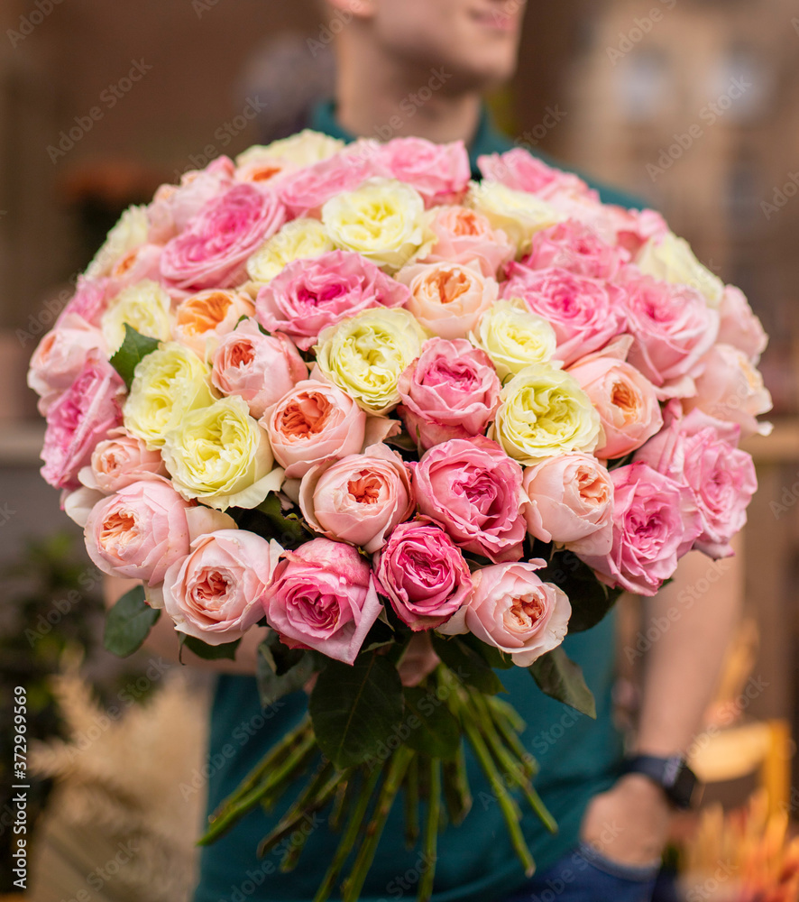 Obraz premium Man with bunch of pink and yellow roses. Young man holding a big bouquet of pink and yellow peonies roses in Women's day. Fresh roses flowers.