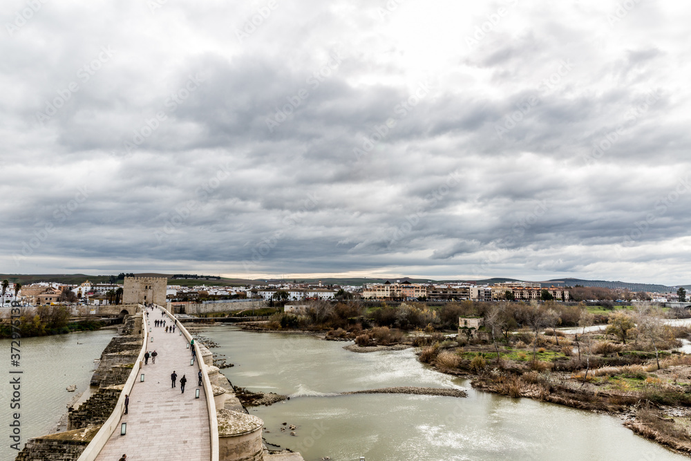 Aerial view of the river Guadalquivir river and the Roman bridge of Cordoba with the city in the background in a wonderful day with a sky full of gray and white clouds in Spain