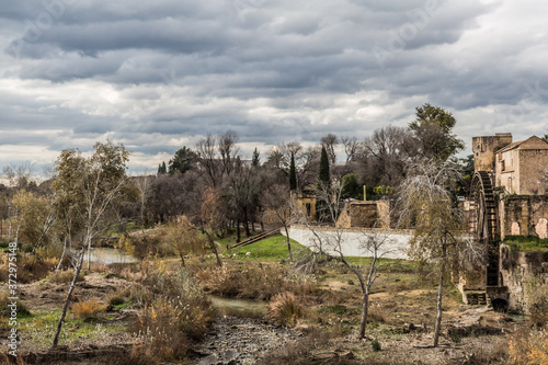 Stream between an arid ground with dry trees next to the ruins of the water mill of Albolafia with a sky covered with gray and white clouds in Cordoba Spain photo