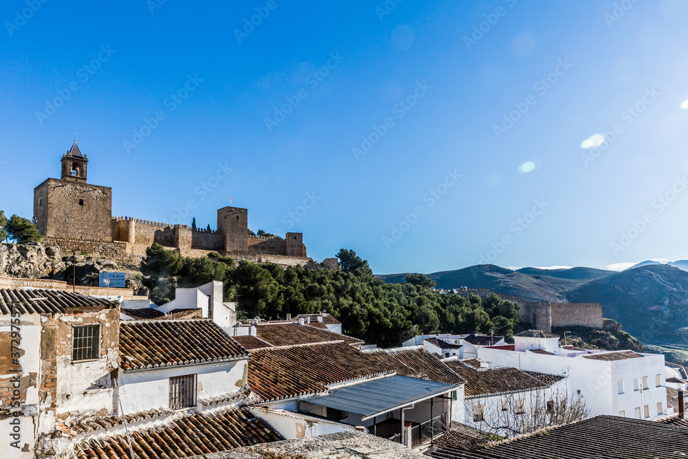 Cityscape with white houses and tile roofs with the Alcazaba de Antequera in the background, wonderful sunny day with a blue sky in the province of Malaga Spain