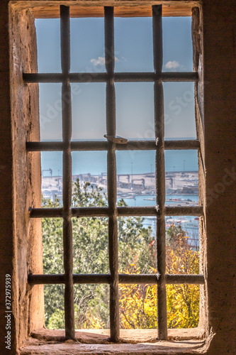 View of the bay of Malaga through a window with wrought iron bars with a padlock in Gibralfaro castle, sunny day with a blue sky in Spain