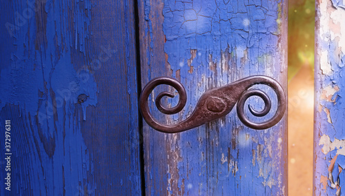 An old blue wooden door with antique metal door handle is opening to a blurred magic alley with spotlights and sunbeams. 