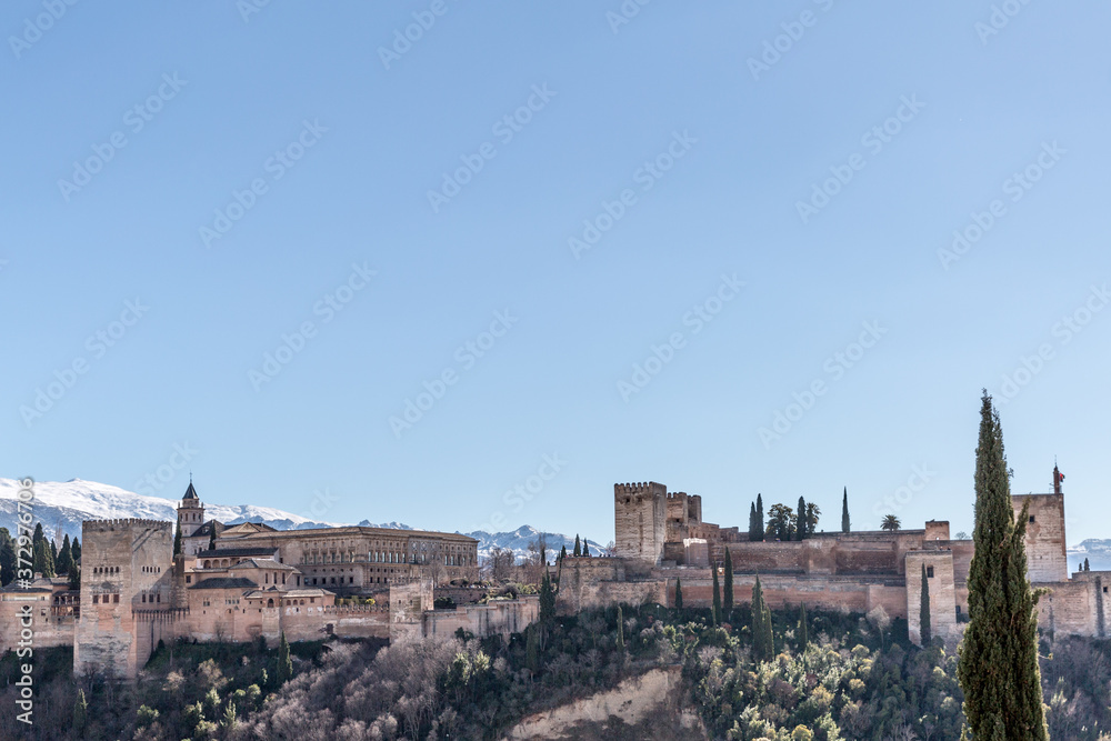 Alhambra on a hill with arid terrain with a snowy mountain in the background on a wonderful sunny day with a blue sky in Granada Spain