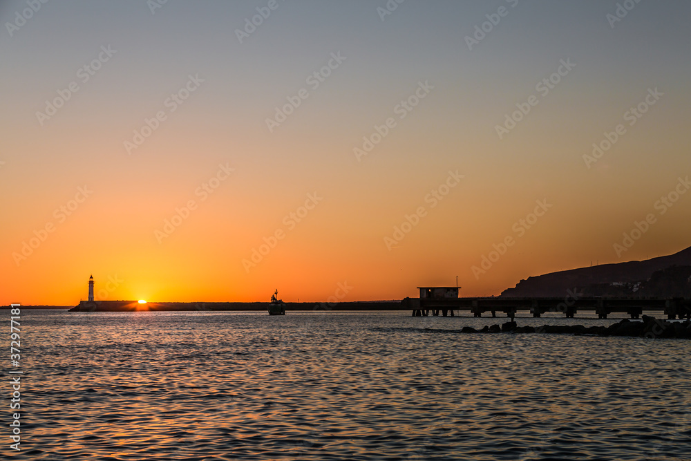 Sunset on the coast of Almeria with a lighthouse and a small boat sailing in the background, relaxing afternoon in Spain