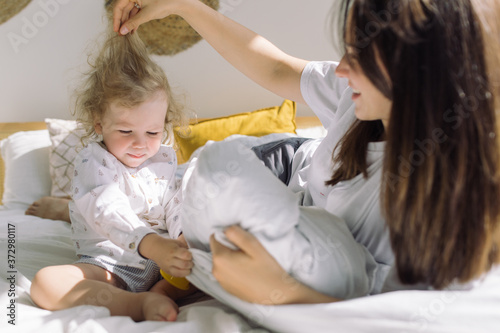 Little cute boy with curly hair playing with mother in bed in the morning. Family moments concept.