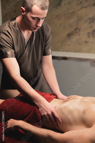 A physiotherapist massager man activates a diaphragm massage to a muscular client male athlete. Close-up. Small depth of field