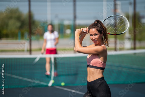 Sportive caucasian woman posing with a racket on a tennis court outdoors.