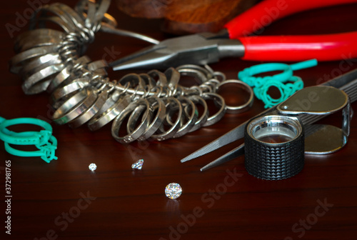 Round white diamonds, magnifying glass , green wax mold, metal ring size, pliers,clamp,tool are used in the manufacture of jewelry.