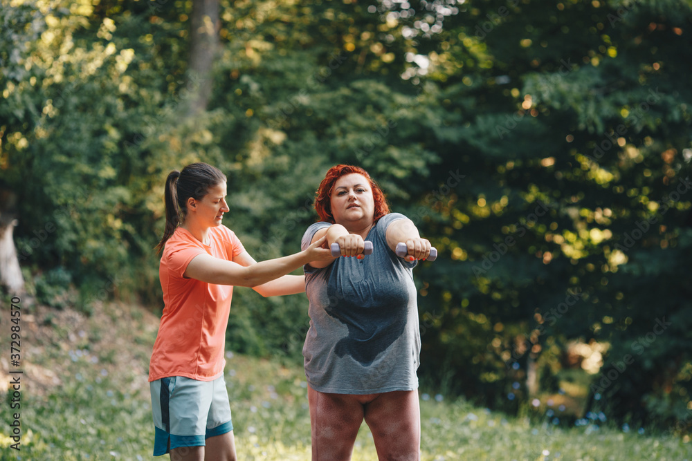 Fototapeta premium An obese woman does weight loss training, arm strengthening exercises, the trainer shows how to do it