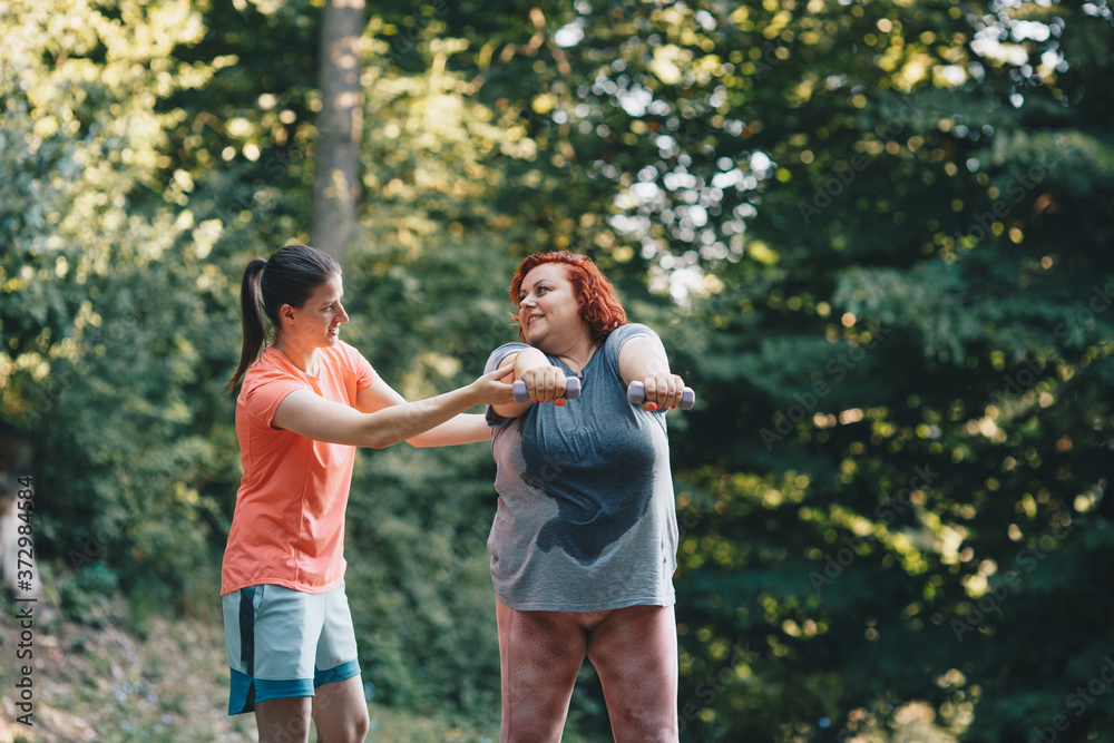 Fototapeta premium An obese woman does weight loss training, arm strengthening exercises, the trainer shows how to do it properly