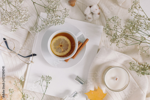 Autumn cozy still life with cup of tea, gypsophila, cashmere scarf, yellow leaves, candle, glasses, perfume. Top view, lifestyle blog concept.