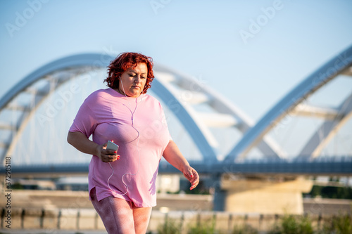 An obese woman listens to music and walks on a treadmill on a sunny day