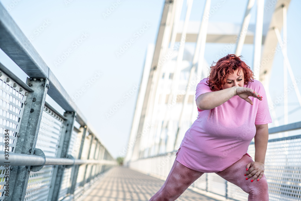 An obese woman does leg stretching exercises and wipes sweat from her forehead with her hand An obese woman does leg stretching exercises and wipes sweat from her forehead with her hand