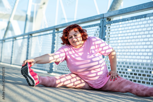 An obese woman does leg stretching exercises during overweight training