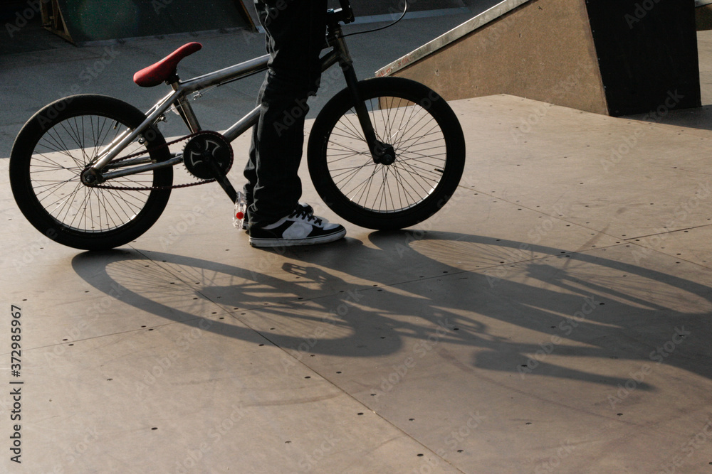 closeup of a young male standing by his bmx bicycle showing only his legs and beautiful shadow on the ground symbolizing youth culture and lifestyle closeup of a young male standing by his bmx bicycle showing only his legs and beautiful shadow on the ground symbolizing youth culture and lifestyle